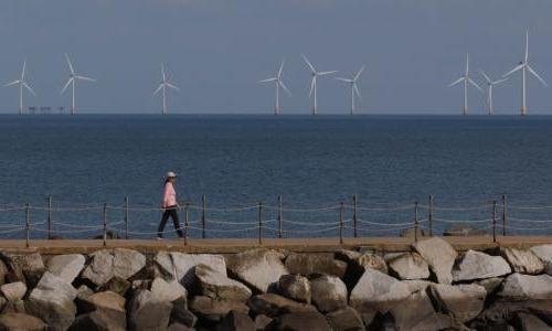 一个人走在一条小路上，背景中可以看到海上风力涡轮机.